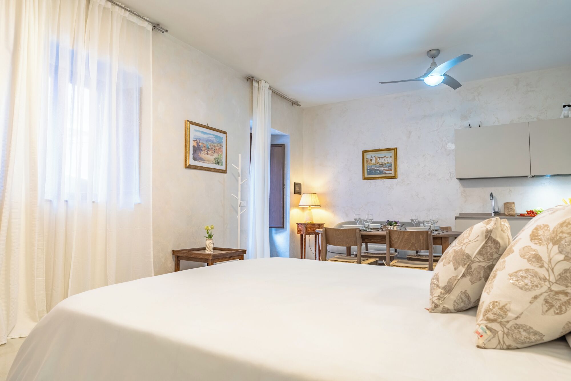 A hotel room with a bed, a desk, a chair, a lamp, and a ceiling fan.