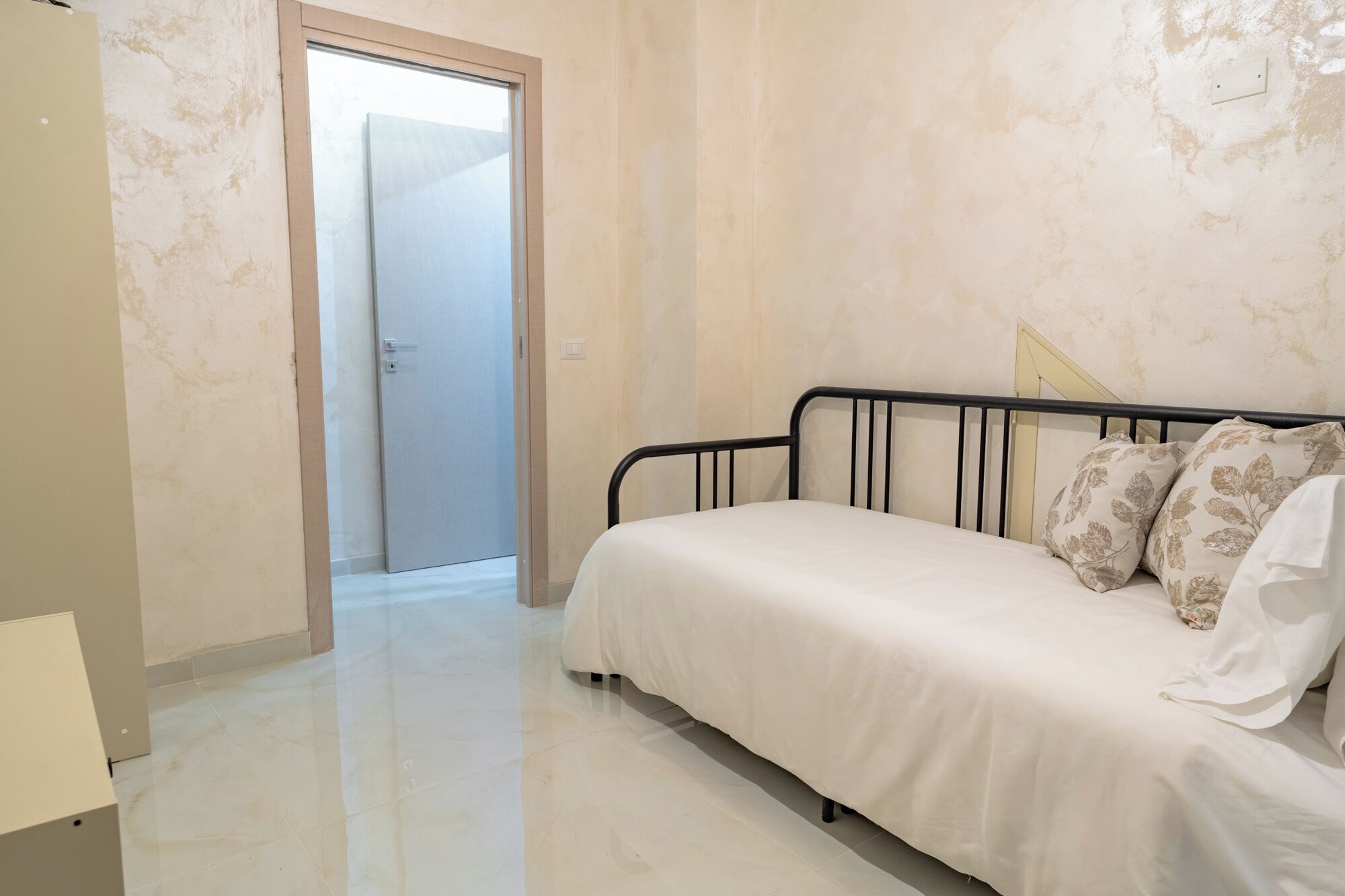 A bedroom with a bed, a door, and a light switch on the wall.
