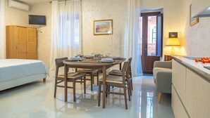 Quarto de hotel com uma cama, uma mesa de jantar para dois, cozinha e vista para a rua.