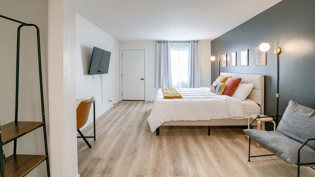 A modern bedroom with a bed, a chair, a TV, and a shelf.