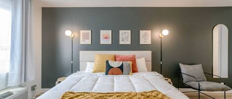 A bedroom with a bed, bedside lamps, a chair, and wall art.