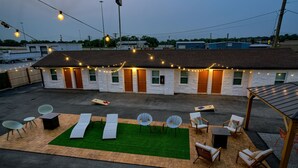 A small white building with a flat roof, a green lawn, and outdoor seating with tables and chairs.