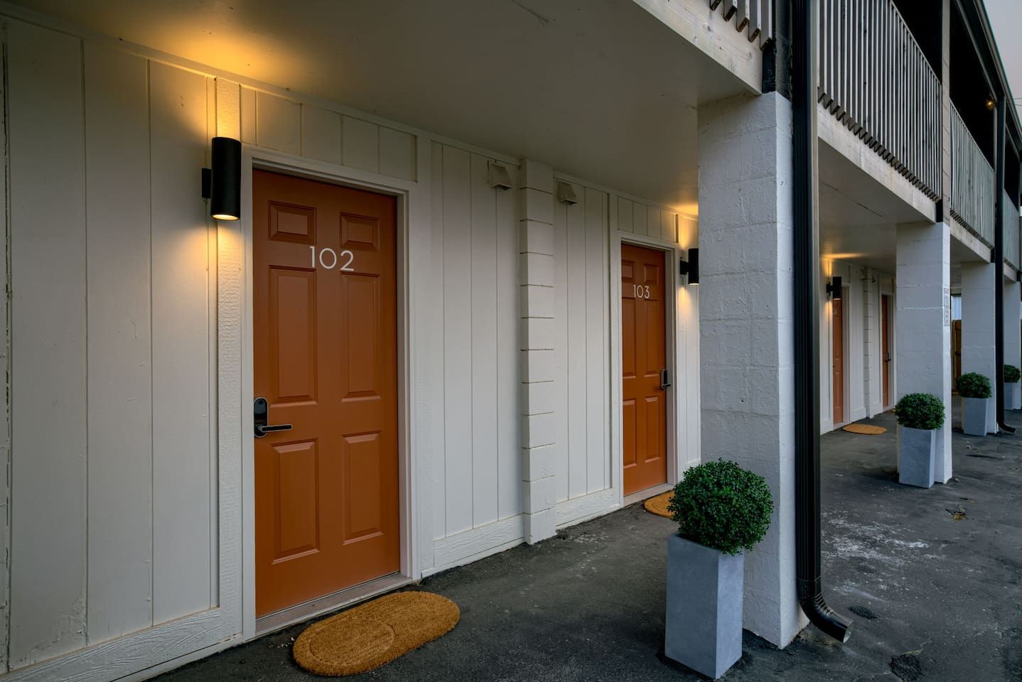 A hotel entrance with two doors, numbered 102 and 103, and a small potted plant beside each door. - Room 101 - King, NonSmoking (Lincoln)