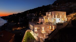 Un moderno edificio a più piani con una terrazza sul tetto, una piscina e vista sul mare al crepuscolo.