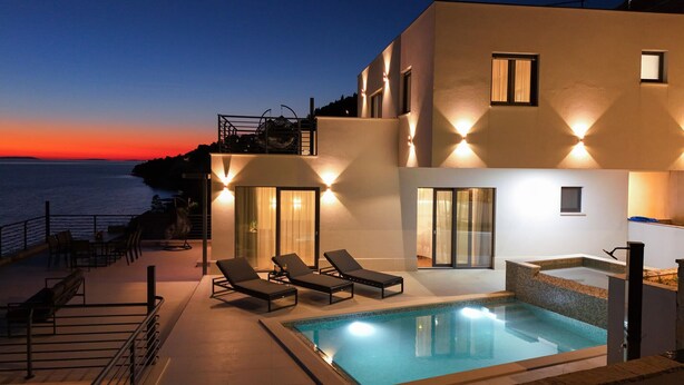 Un edificio moderno con piscina, lettini e vista sul mare al tramonto.