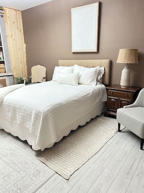 A bedroom with a bed, a nightstand, a chair, a lamp, and a wall-mounted picture.