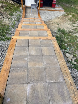 A wooden deck leading to a door, with a gravel path and a chair nearby.