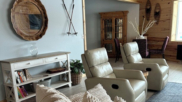 A cozy living room with a wooden ceiling, a large round mirror, a bookshelf, and two leather sofas with matching cushions.