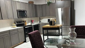 A modern kitchen with grey cabinets, a microwave, a stove, and a refrigerator. There is a dining table with chairs and a vase on it.