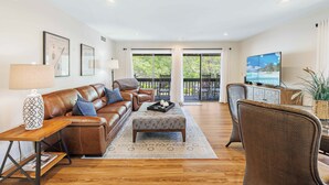 A spacious living room with a brown leather sofa, a wooden coffee table, and a wicker chair. - Lakefront Pinehurst Condo 2BD/2BA - 237 - With Community Pool Access (Pinehurst)