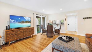 A spacious living room with a wooden floor, a television, a dining area with chairs, and a kitchen in the background. - Lakefront Pinehurst Condo 2BD/2BA - 237 - With Community Pool Access (Pinehurst)
