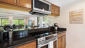 A modern kitchen with stainless steel appliances, wooden cabinets, and a large window providing a view of the outdoors. - Lakefront Pinehurst Condo 2BD/2BA - 237 - With Community Pool Access (Pinehurst)