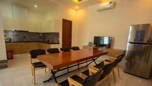 A modern kitchen with a dining area, equipped with a stainless steel refrigerator, a flat-screen TV, and a wooden dining table with chairs.
