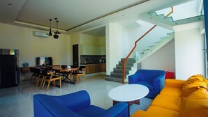 A modern living room with a staircase, a dining area, and a kitchen.