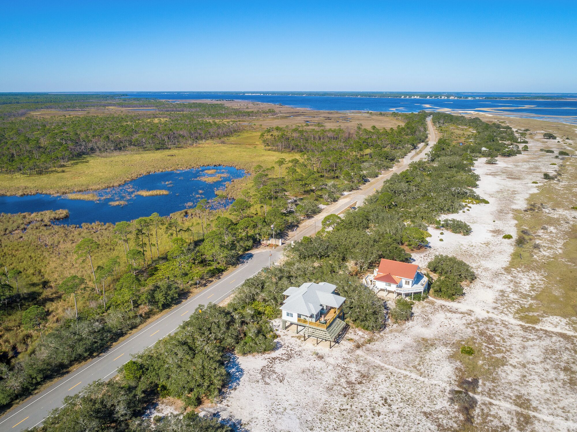 An aerial view of a coastal property with a road, a large body of water, and dense vegetation.