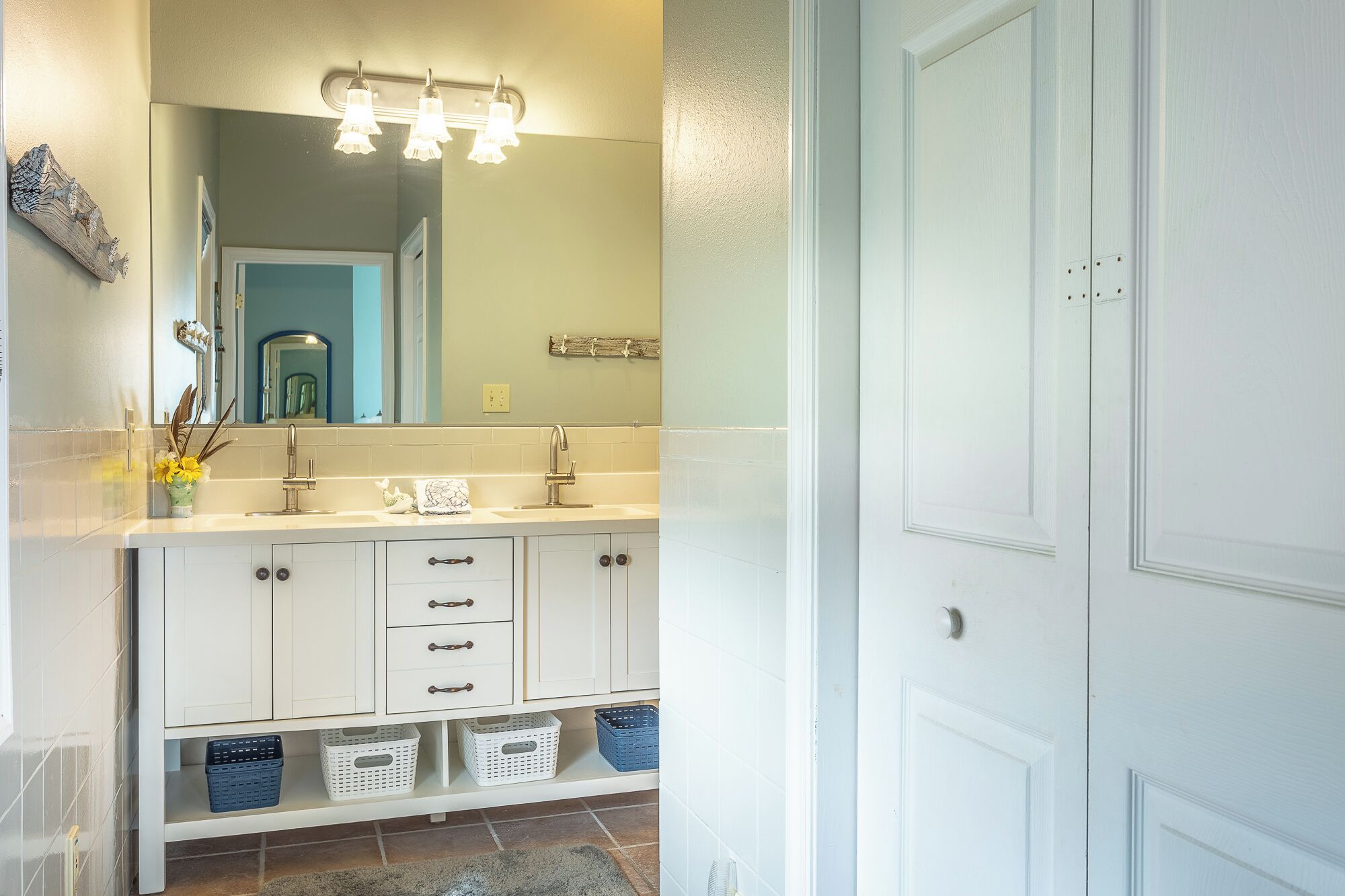 A bathroom with a white vanity, two sinks, a mirror, and a towel rack.