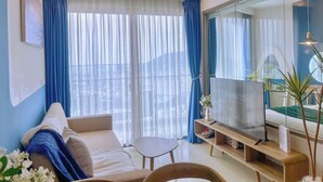 Un salon moderne avec un canapé, une table basse, un téléviseur posé sur un meuble et une grande fenêtre ornée de rideaux bleus.