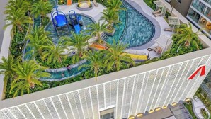 Un espace piscine aménagé sur le toit, agrémenté de palmiers, d’un toboggan bleu et d’une fontaine circulaire.