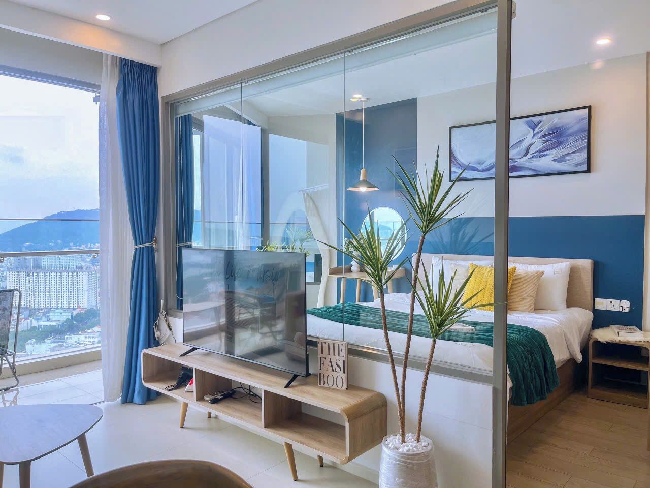 Habitación de hotel moderna con un televisor grande, un sofá, una cama y un balcón con vistas a la ciudad.