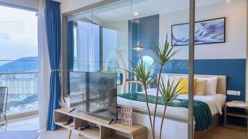 Habitación de hotel moderna con un televisor grande, un sofá, una cama y un balcón con vistas a la ciudad.