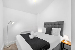 Un dormitorio moderno con una cama grande, una mesita de noche con lámpara, una lámpara de pie y un radiador.