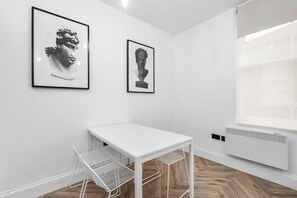 Una habitación minimalista con una mesa blanca, dos obras de arte enmarcadas, un radiador y una ventana.