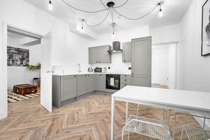 Una cocina moderna con armarios grises, encimera blanca y suelo de madera en espiga.