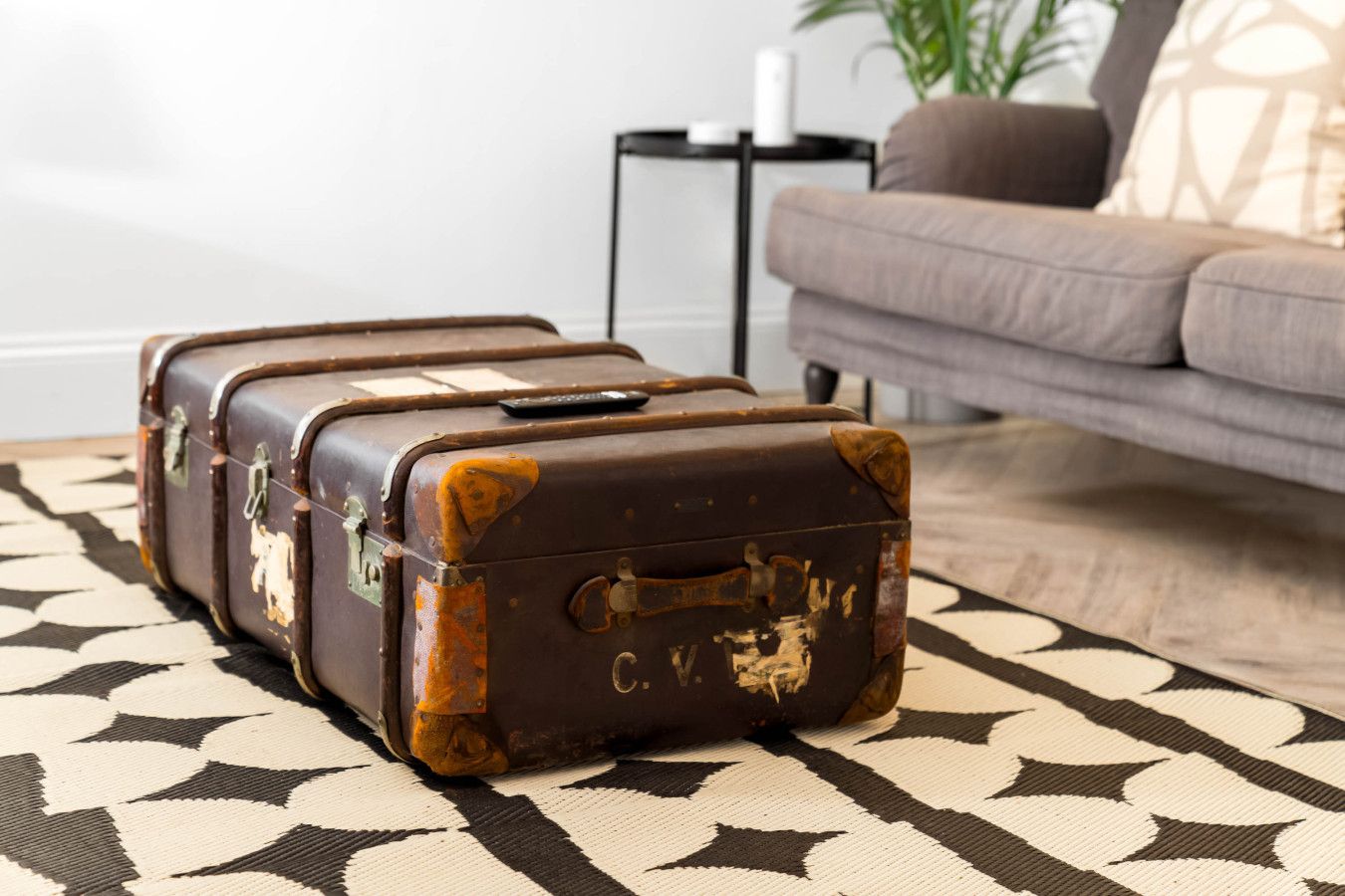 A vintage suitcase with a lock and a handle, placed on a patterned rug in a living room.