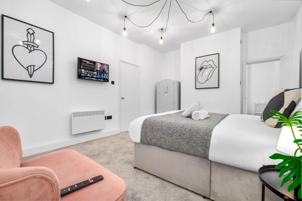 A modern bedroom with a bed, a TV, a chair, and a plant.