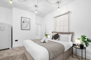 Ein modernes Schlafzimmer mit einem großen Bett, Nachttischen, einem Fenster mit Jalousien und einer Wandleuchte.