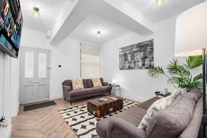 A modern living room with a sofa, a coffee table, and a painting on the wall. - Modern 3 Bedroom Townhouse - Bedroom TVs - Wolverhampton Centre (Wolverhampton)