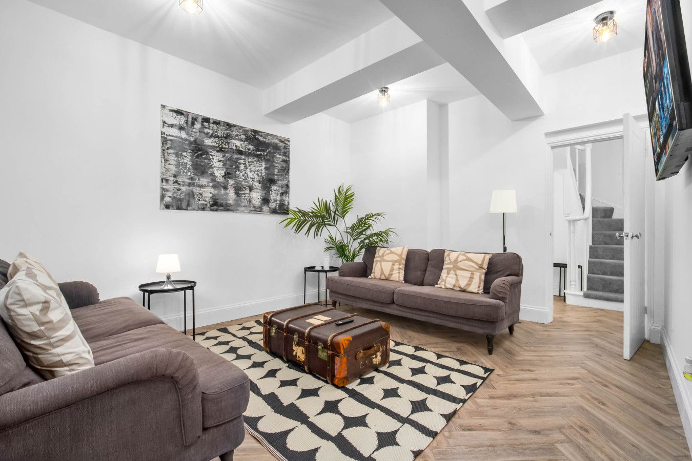 Uma sala de estar moderna com um sofá cinza, um tapete estampado, um baú antigo e um grande quadro abstrato na parede.