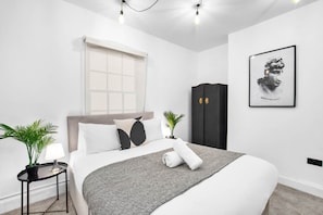 A modern bedroom with a bed, bedside table, lamp, potted plant, and a wardrobe. - Modern 3 Bedroom Townhouse - Bedroom TVs - Wolverhampton Centre (Wolverhampton)
