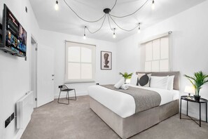 Un dormitorio moderno con una cama grande, una silla, un escritorio y un televisor mostrando opciones de películas.