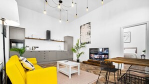 Una sala moderna con un sofá amarillo, una mesa de centro blanca y un comedor con mesa de madera y sillas de metal.