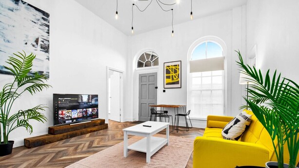 Una sala moderna con un televisor de pantalla plana grande, un sofá amarillo, una mesa de centro blanca y un comedor con mesa y sillas.