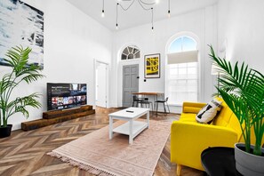 Un salon moderne doté d’un grand téléviseur à écran plat, d’un canapé jaune, d’une table basse blanche et d’un coin repas avec une table et des chaises.