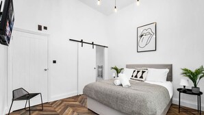 Un dormitorio moderno con una cama grande, una lámpara colgante, una obra de arte enmarcada y un suelo de madera con diseño de espiga.