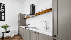 Una cocina moderna con encimera blanca, armarios grises, un lavamanos de acero inoxidable y una campana extractora negra.