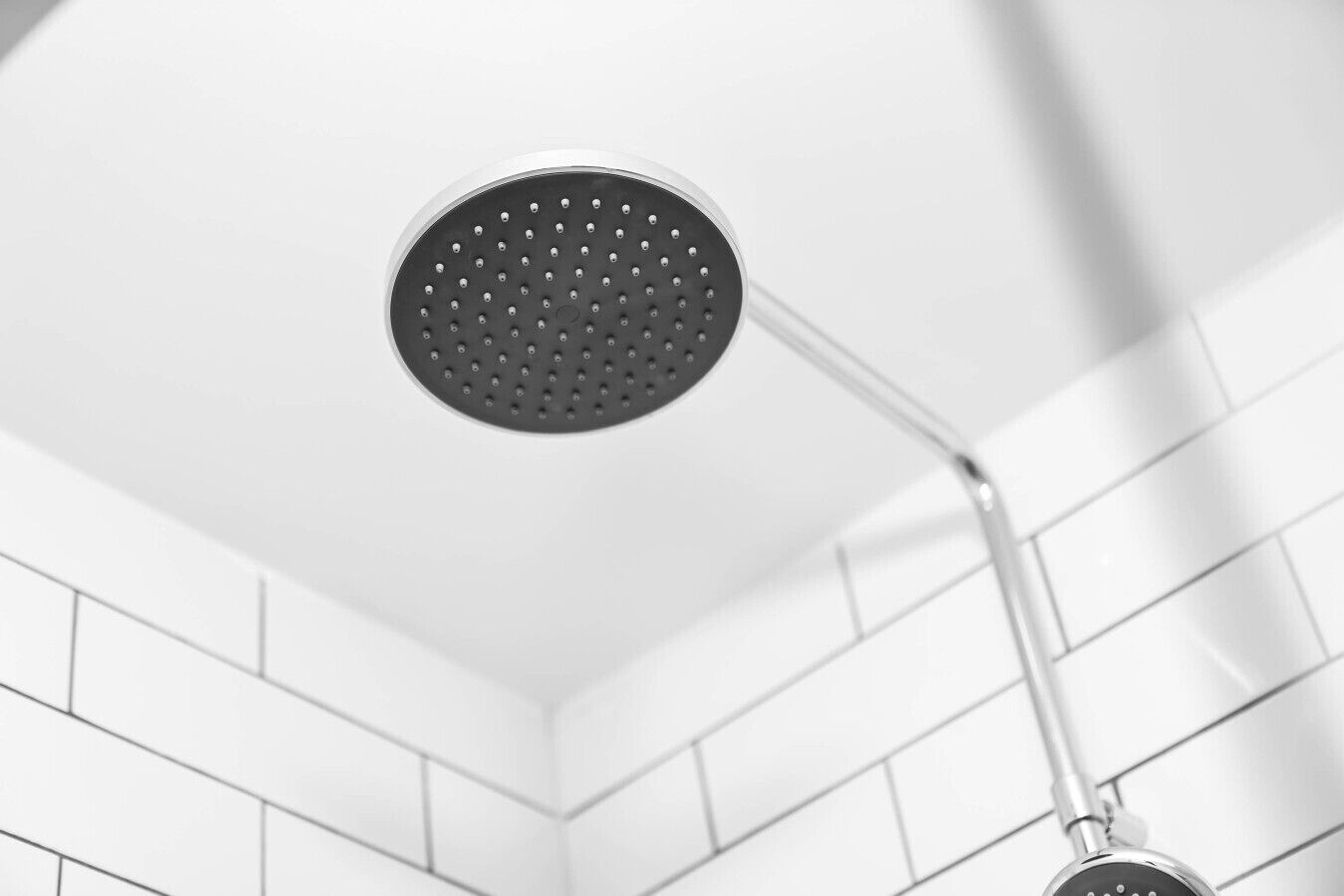 Un cabezal de ducha con diseño redondo y perforado, instalado en una pared con azulejos blancos.