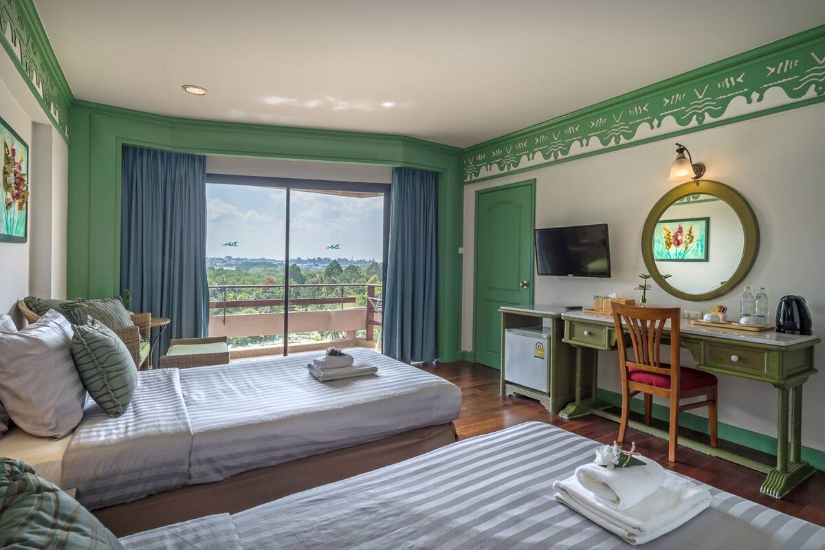 A hotel room with two beds, a desk, a chair, a television, and a balcony with a view of the landscape.