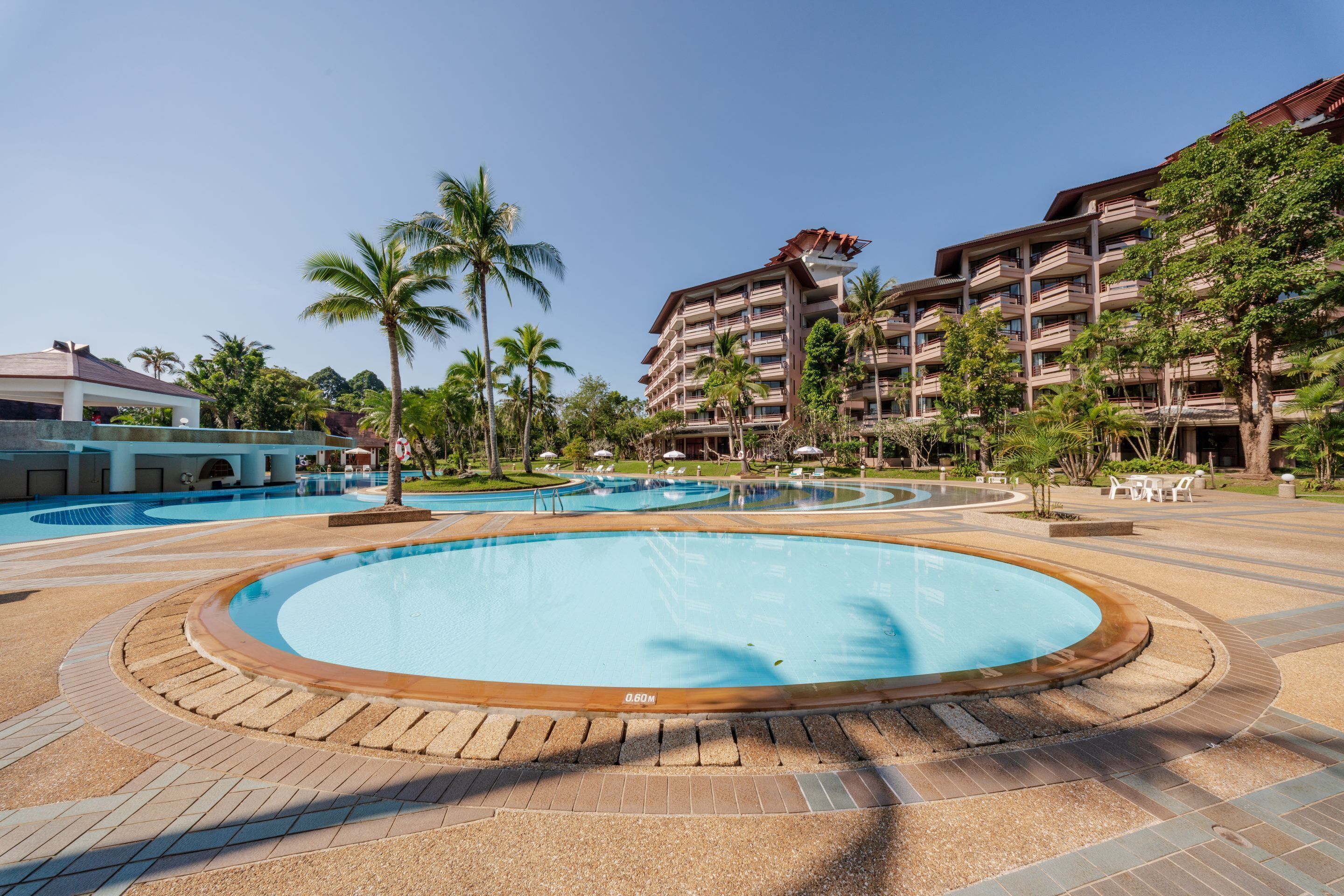 Een resort met diverse zwembaden, palmbomen en een groot gebouw met balkons.
