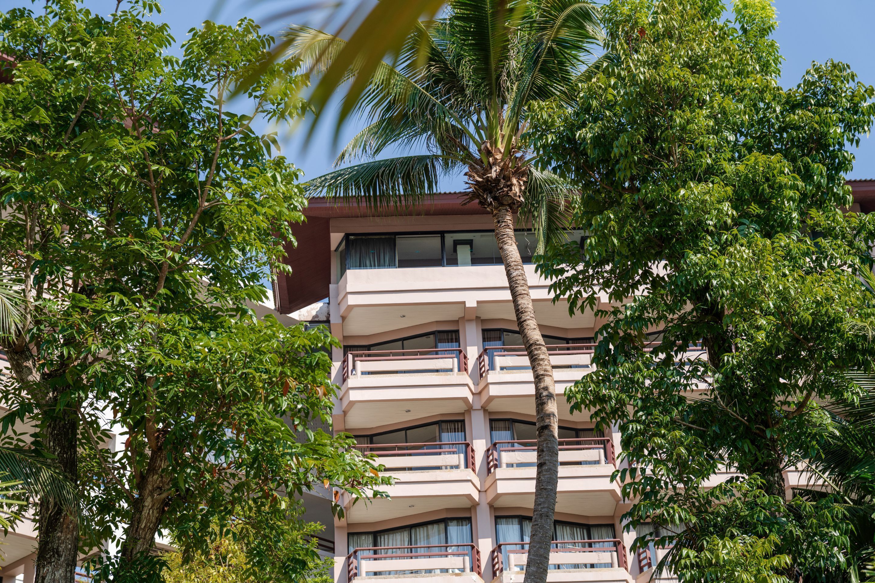 Un edificio de varios pisos con balcones, rodeado de exuberantes árboles verdes.