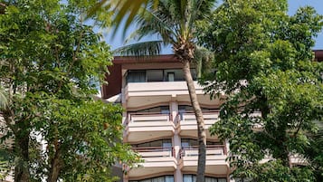 Un edificio de varios pisos con balcones, rodeado de exuberantes árboles verdes.