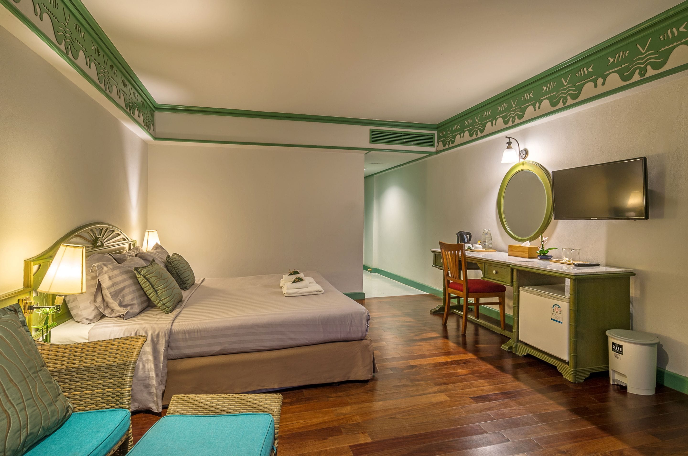 A hotel room with a bed, a desk with a mirror, a TV, and a waste bin.