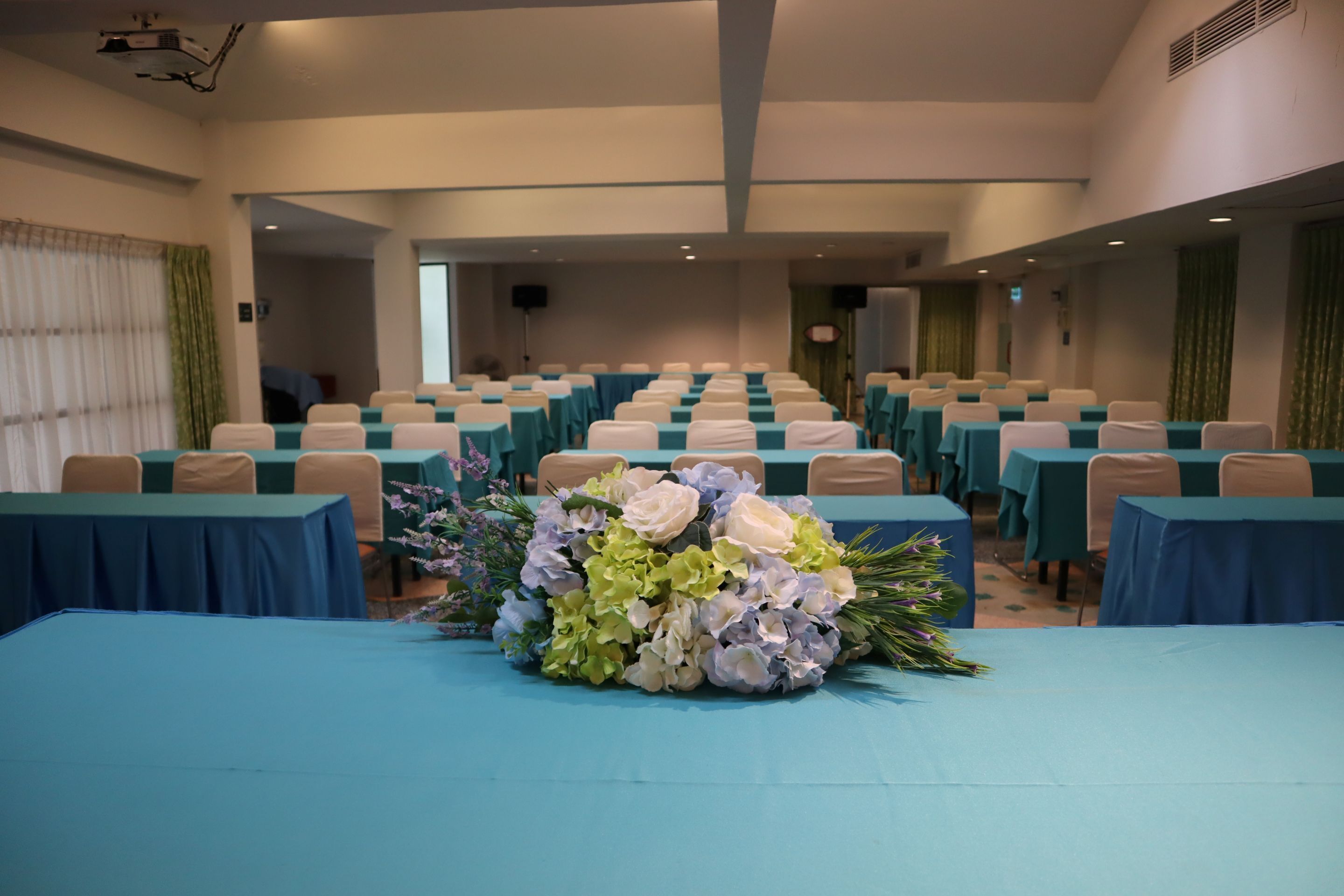 A conference room with rows of tables, chairs, and a floral centerpiece.