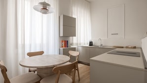 A modern kitchen with a round dining table, wooden chairs, a hanging light fixture, and a built-in oven. - Tornabuoni Dream By MMega (Firenze)