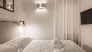 A hotel room with a neatly made bed, a wall-mounted light fixture, and a large window with sheer curtains. - Tornabuoni Dream By MMega (Firenze)