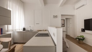 A modern kitchen with a built-in oven, a sink, and a countertop. There is a dining area with a table and chairs, and a living space with a sofa and a plant. - Tornabuoni Dream By MMega (Firenze)