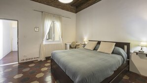 Un dormitori amb un llit gran, un escriptori, una cadira, una finestra amb cortines i un radiador.